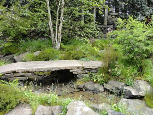 Foto: BGL. - Bei dieser Gartengestaltung wird aus Naturstein ein Bachlauf mit Brücke angelegt, der Regenwasser sammelt und bei Bedarf für die Bewässerung der Beete genutzt werden kann.